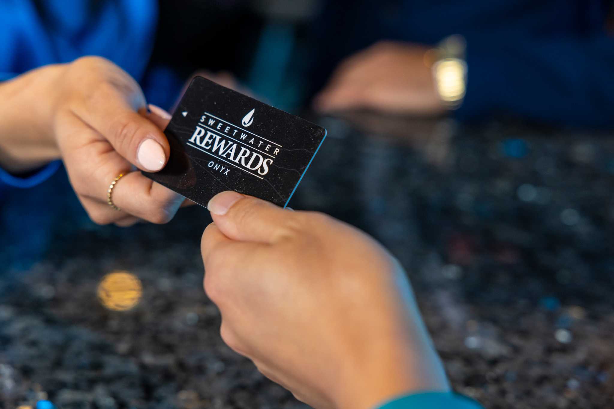 A person is being handed the Sweetwater Rewards -Onyx- card.